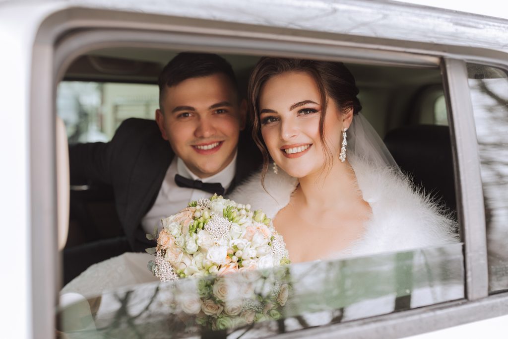 Beautiful bride and groom looking at the camera while sitting in a stylish white car. Beautiful wedding. Smiling wedding couple